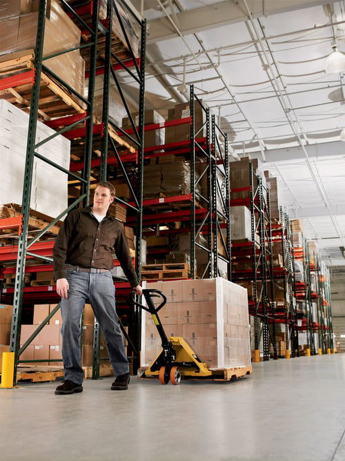 Ground level view of man pulling Caterpillar pallet jack through warehouse aisle